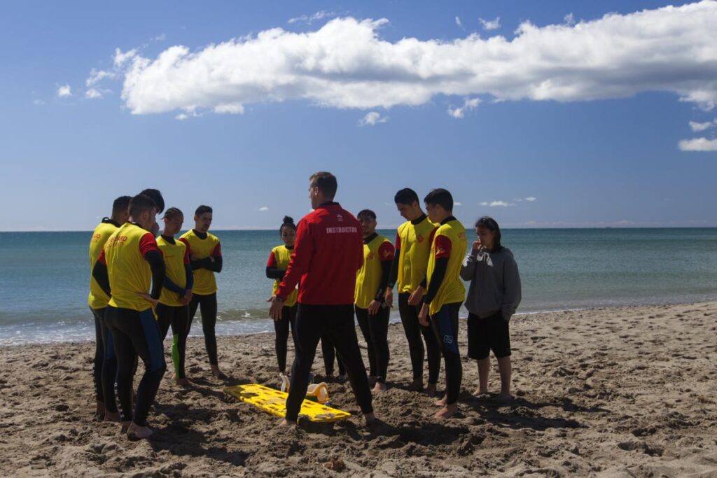 Instructor de Grupo FASST explicando a alumnos de socorrismo cómo atender a una víctima en la playa